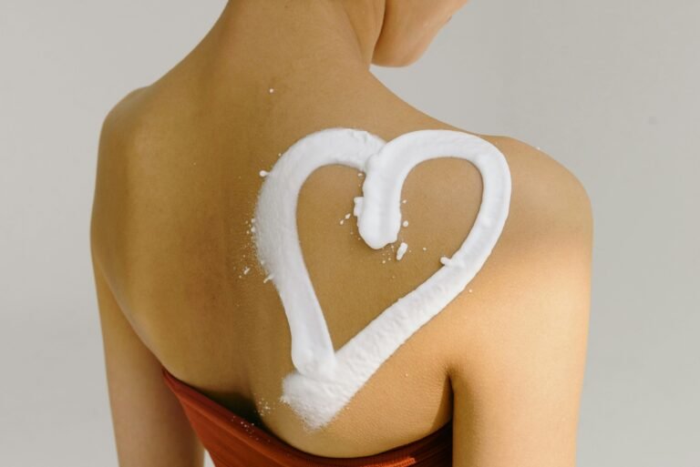 Rear view of a woman's shoulder with a heart shape drawn in cream, symbolizing love and skincare.